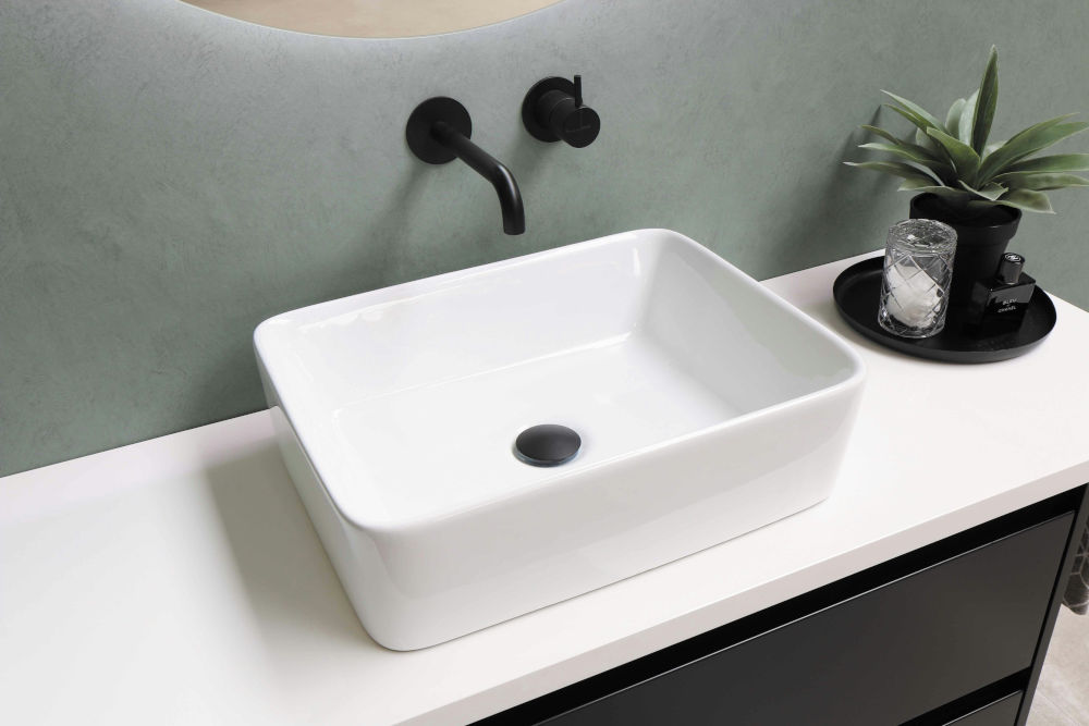 A white sink sitting on top of a fixed unit with black taps and sink hole.